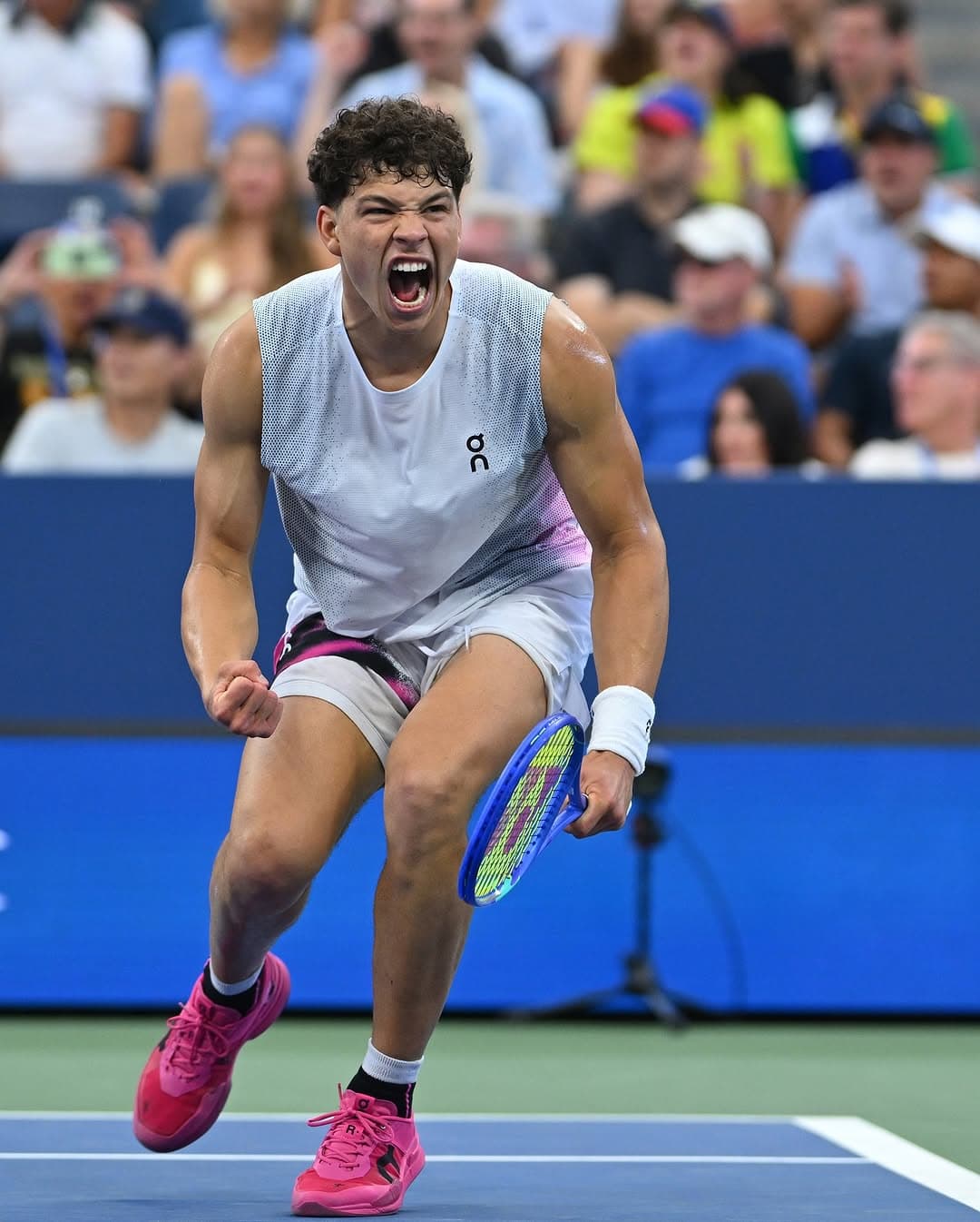 Ben Shelton celebrates with a fist pump and shout on blue hard court, pink shoes and On logo visible.