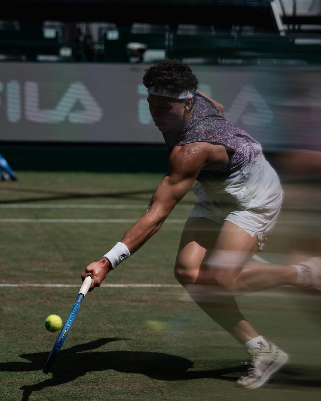 Ben stretches low to hit a forehand on grass court, focused and athletic stance.